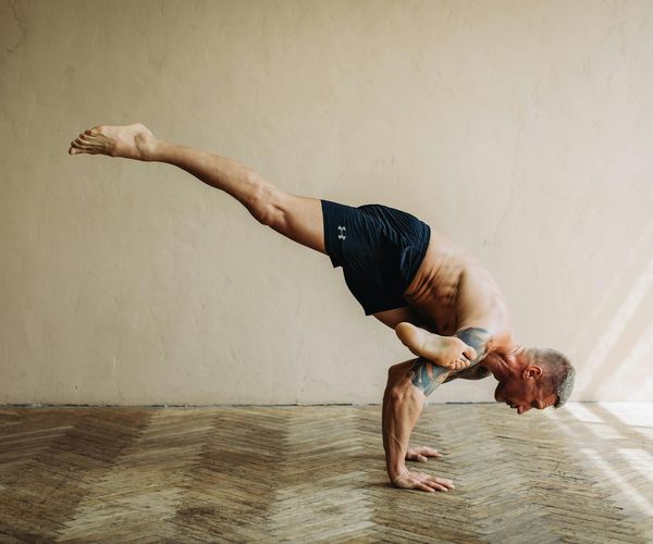 Man holding a difficult arm-balance yoga pose, showcasing physical power.